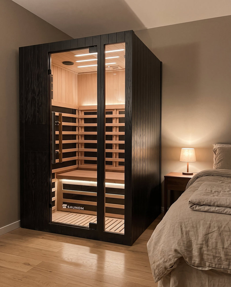 Black Saunom sauna lit from inside, next to a bed