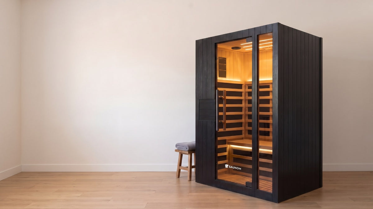 Black Saunom infrared sauna glowing warm inside, standing in a calm spare room in the evening