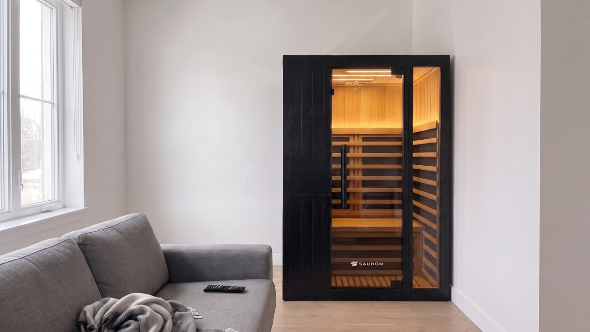 Black Saunom infrared sauna lit warm inside, standing in a lived-in living room in the evening