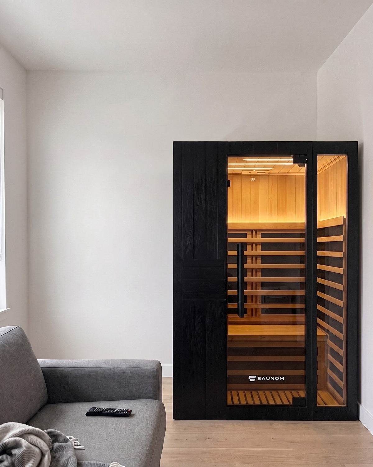 Black Saunom infrared sauna lit warm inside, standing in a lived-in living room in the evening