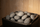 A residential electric sauna heater filled with loosely stacked gray volcanic sauna stones with white speckling, in a warm pale-wood Finnish sauna.
