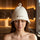 Woman wearing a white merino wool sauna hat while relaxing in a warm wooden sauna