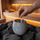 Hand adding a small menthol crystal into a grey sauna aroma stone cup placed among heater rocks
