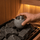 Hand placing a soapstone aromatherapy cup among dark sauna heater stones before it begins to steam