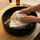 White wool beanie-style sauna hat being gently hand washed in a black sink