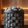 Close-up of rounded sauna stones stacked inside a black heater basket with warm sauna lighting
