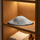 Grey wool sauna hat displayed flat on a wooden shelf with towels and amber bottle