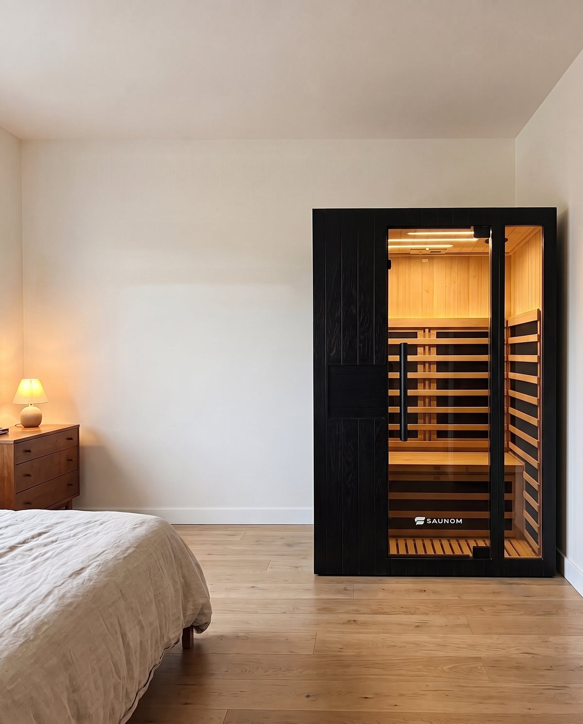 Black Saunom infrared sauna standing in a bedroom next to the bed