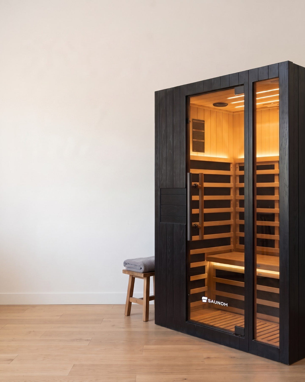 Black Saunom infrared sauna glowing warm inside, standing in a calm spare room in the evening