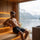 Man relaxing in a modern sauna while wearing a grey wool sauna hat with snowy forest view