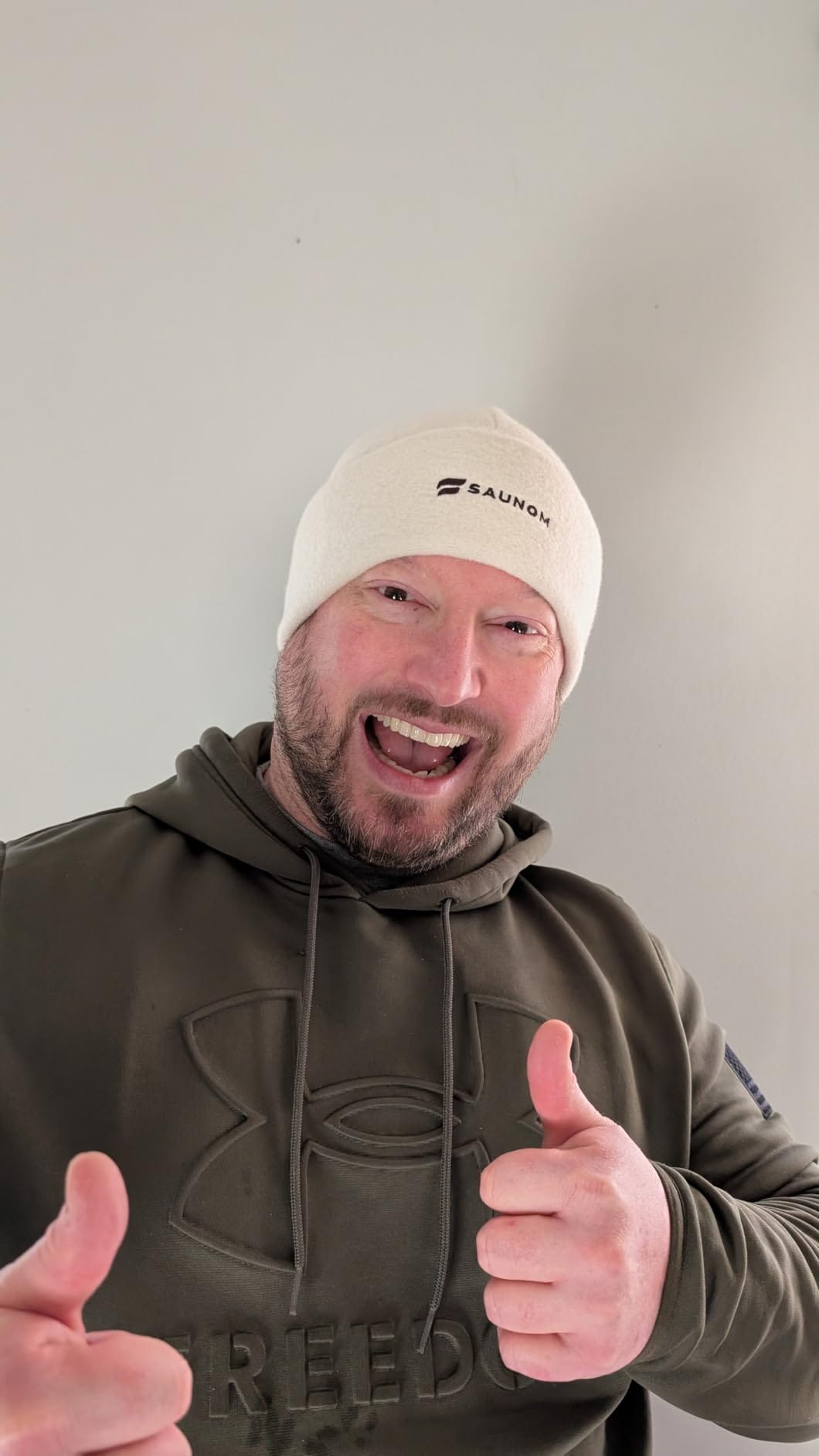 Smiling man wearing a white sauna hat and giving two thumbs up