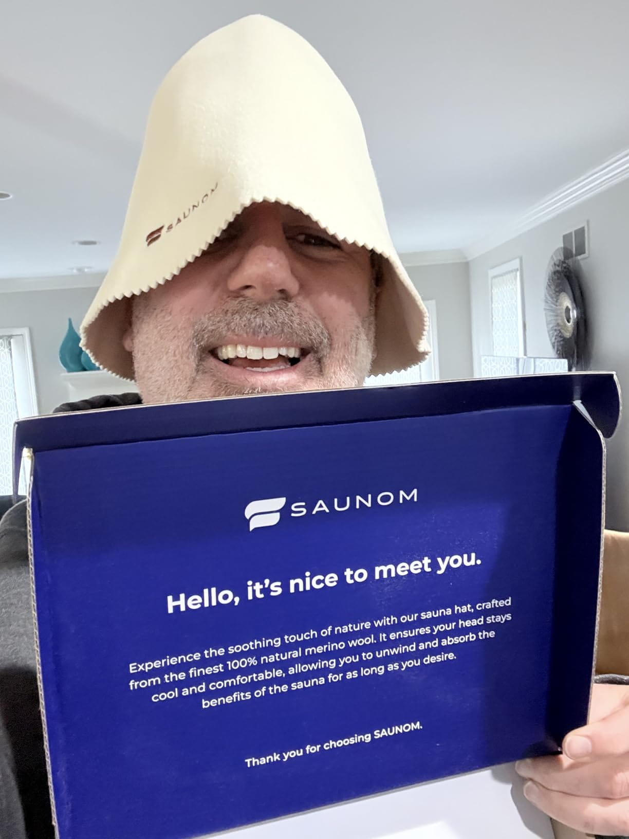 Man wearing a white wool sauna hat while holding SAUNOM product packaging