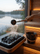 SAUNOM ladle pouring water over sauna rocks beside a matching water bucket with a calm lake view outside