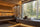 A luxury wooden sauna room with a large floor-to-ceiling window overlooking a dense pine forest, featuring a stone bench with towels and sauna accessories.