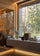 A luxury wooden sauna room with a large floor-to-ceiling window overlooking a dense pine forest, featuring a stone bench with towels and sauna accessories.