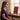 Woman wearing goggles sitting at a desk in front of the Saunom EW300 Pro red light therapy panel, with the light on her face, neck and chest