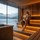 Man sitting in a sauna with a scenic view of mountains and water outside.