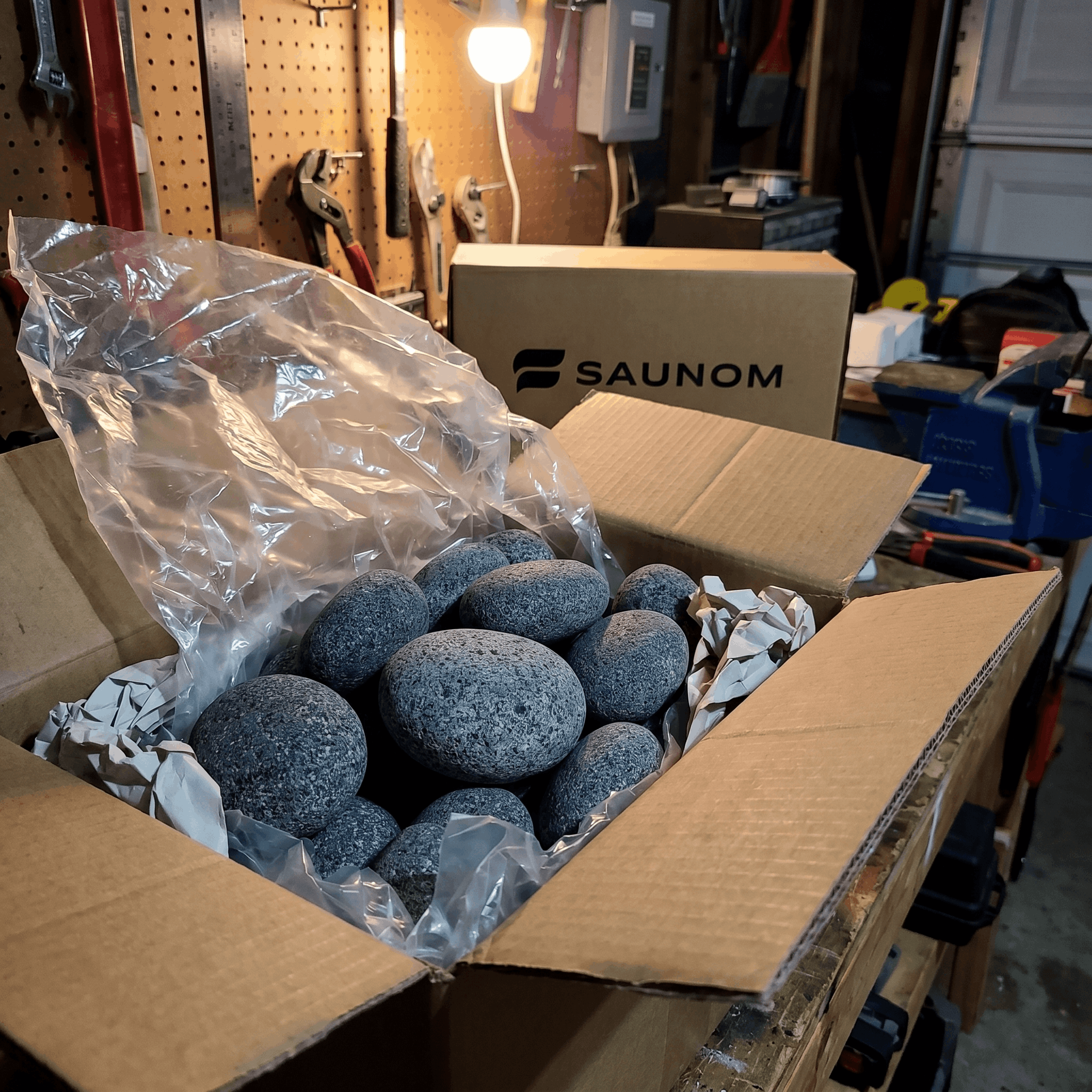 Rounded grey sauna stones packed inside an open shipping box

