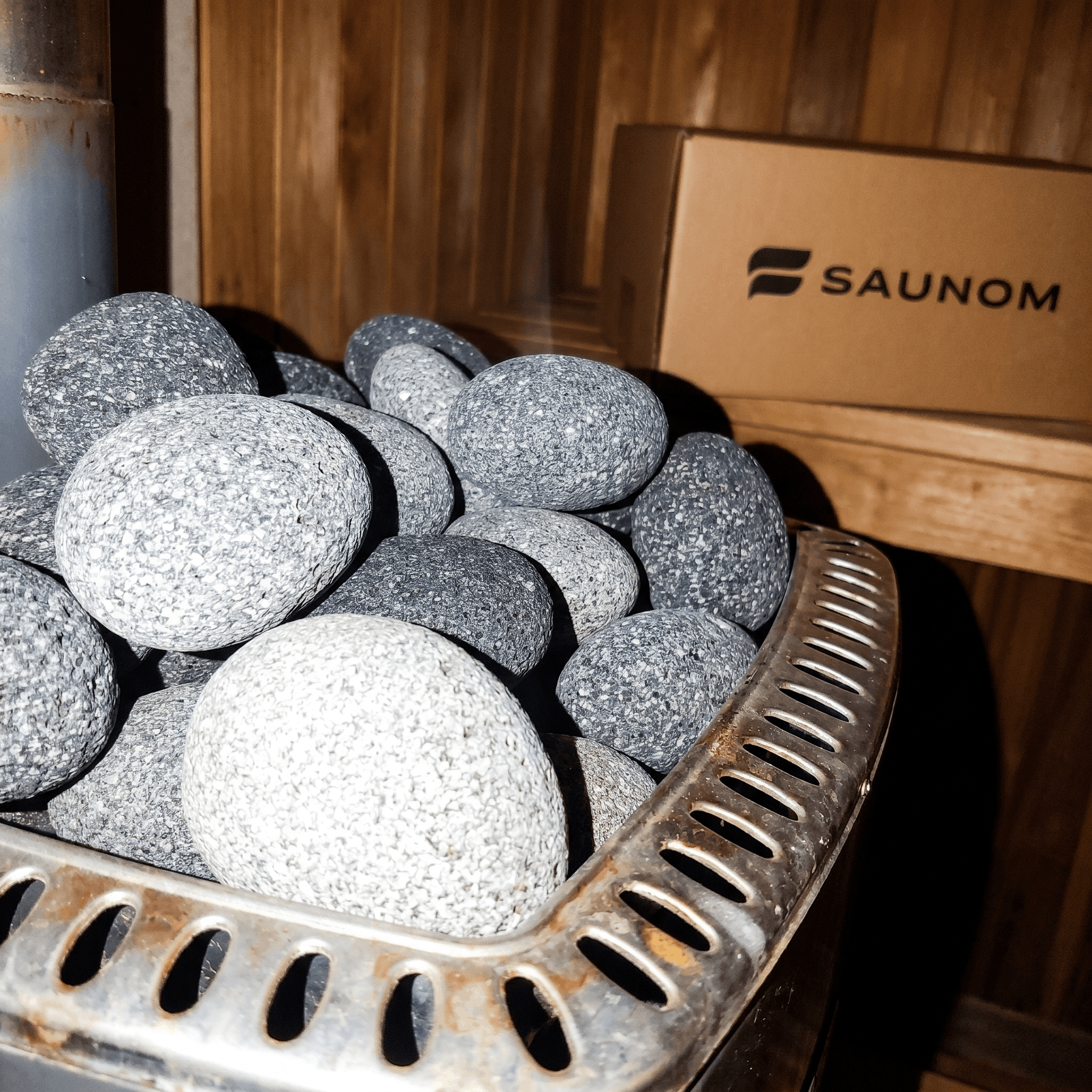 Rounded sauna stones stacked inside a sauna heater with branded packaging in the background