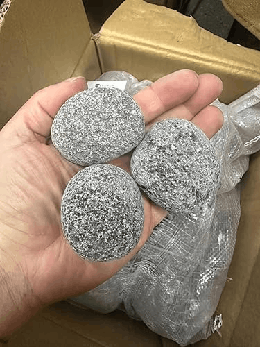 Rounded gray sauna stones held in hand before being placed in a sauna heater