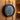Round black sauna thermometer hanging on a wooden sauna wall showing temperature in Fahrenheit