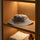 Grey wool bucket-style sauna hat displayed flat on a wooden shelf with towels and amber bottle