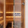 Tempered safety glass door panel with a brushed metal handle and hinge, shown installed in a wooden sauna. The glass features a blue text overlay reading '8 mm TEMPERED SAFETY GLASS'.