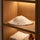 White wool sauna hat displayed flat on a wooden shelf with towels and amber bottle