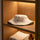 White wool bucket-style sauna hat displayed on a wooden shelf with folded towels and amber bottle