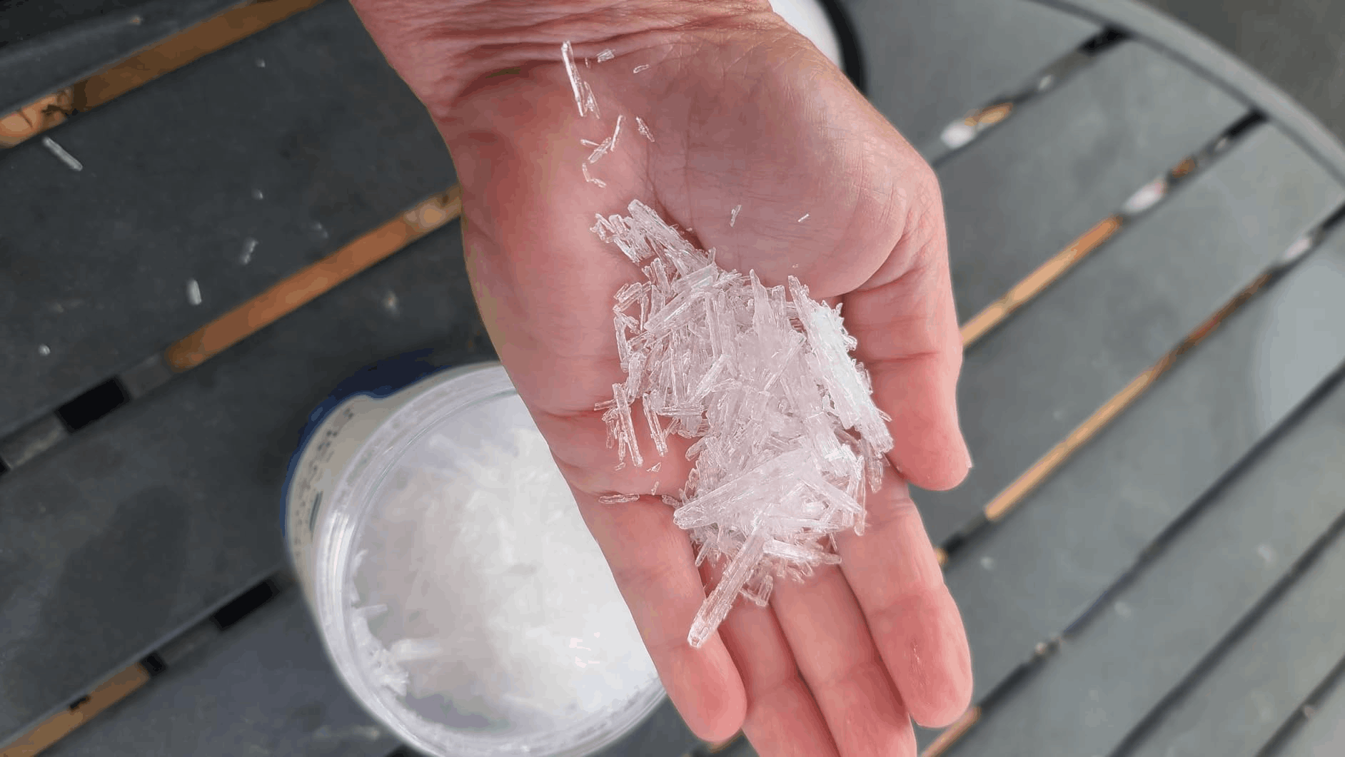 Clear menthol crystals held in hand beside an open jar