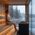 Woman relaxing in a modern wooden sauna with steam rising from the heater and a snowy lake view outside