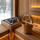 Gold SAUNOM sauna bucket and ladle resting on a wooden sauna bench next to heater stones