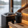 SAUNOM black sauna water bucket held by its bamboo handle, with a matching ladle on the bench beside the heater.