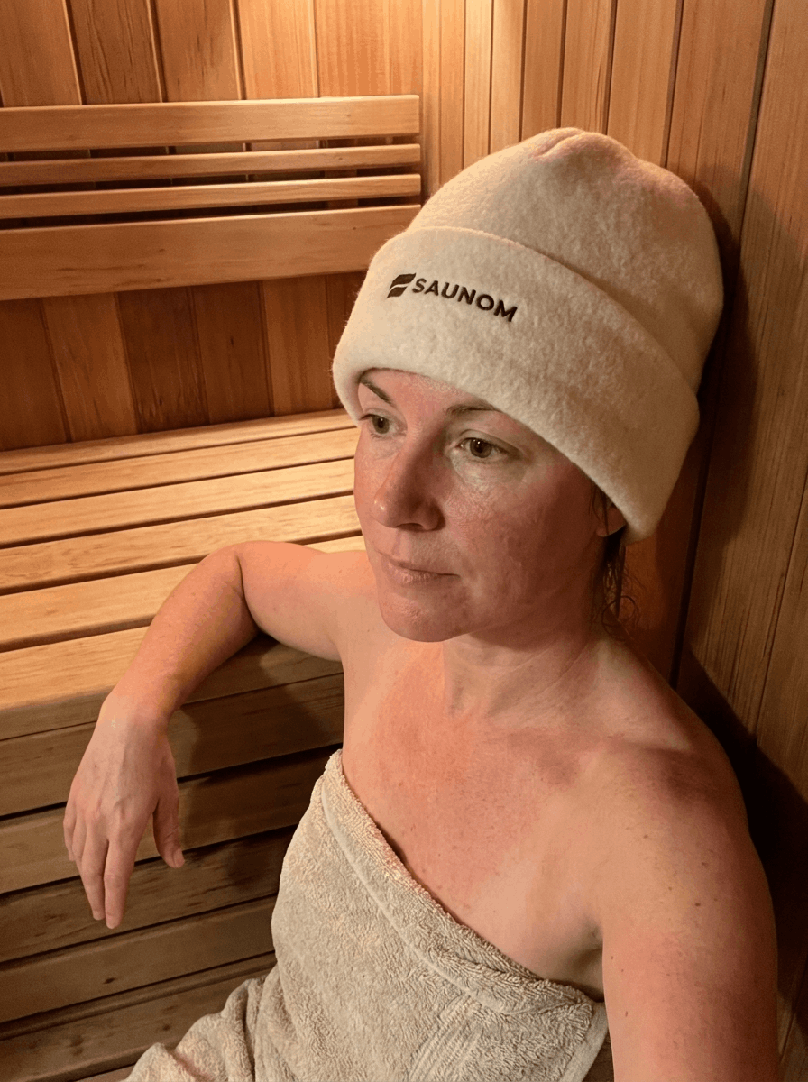 Woman relaxing in a wooden sauna while wearing a white wool sauna hat

