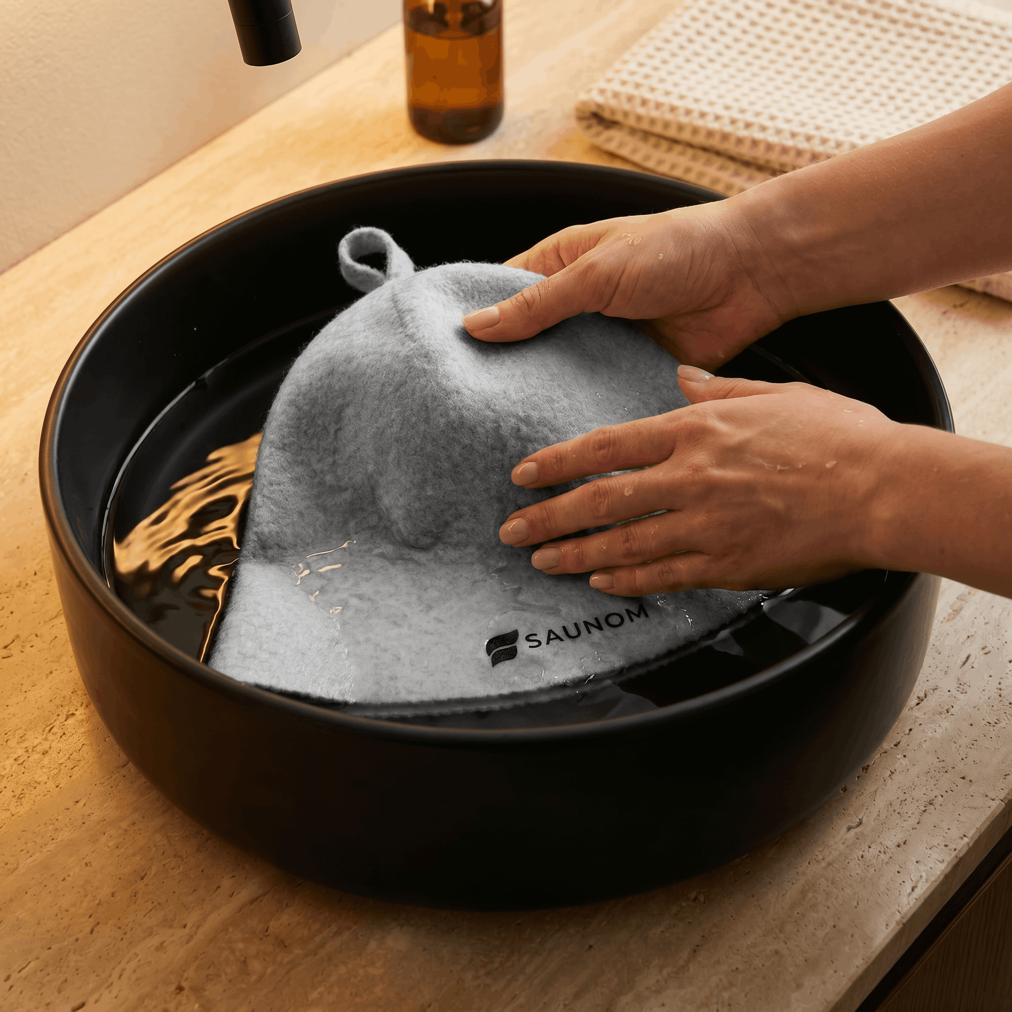Grey wool sauna hat being gently hand washed in a black sink
