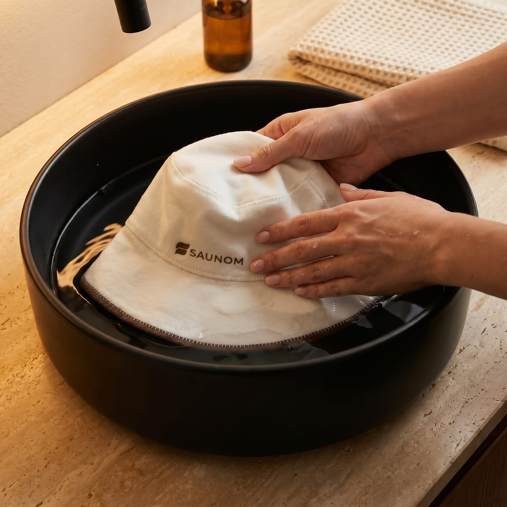 White wool bucket-style sauna hat being gently hand washed in a black sink