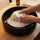 White wool bucket-style sauna hat being gently hand washed in a black sink