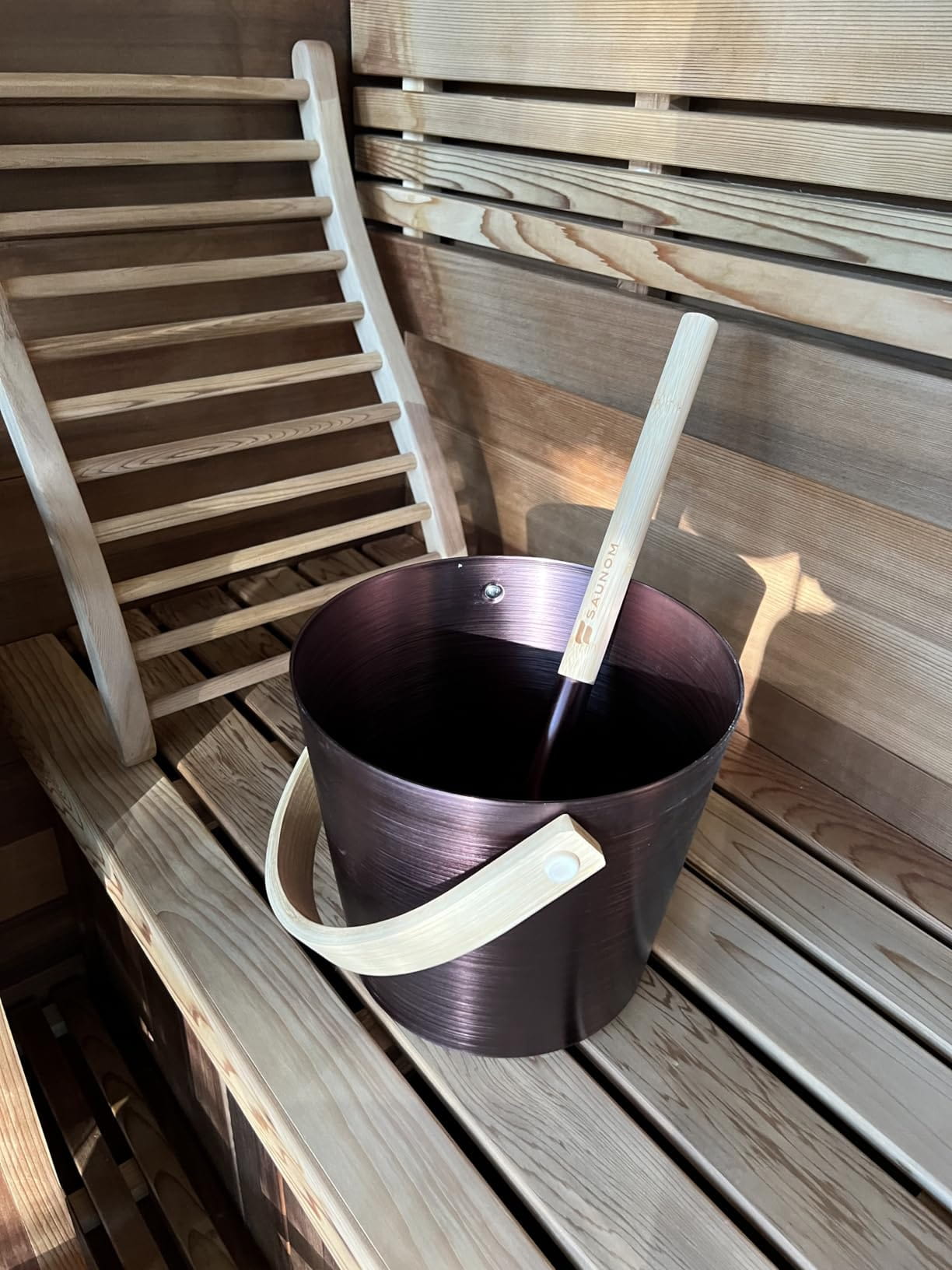 Dark sauna bucket with wooden handle and matching ladle on a wooden sauna bench