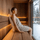 Side view of a woman sitting comfortably in a sauna supported by a curved SAUNOM wooden backrest