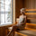 Woman wearing a white sauna hat while looking out from a warm wooden sauna toward a snowy forest